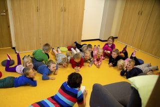 Lapsia makaamassa Linnoituksen päiväkodin lattialla opettajan johdolla.