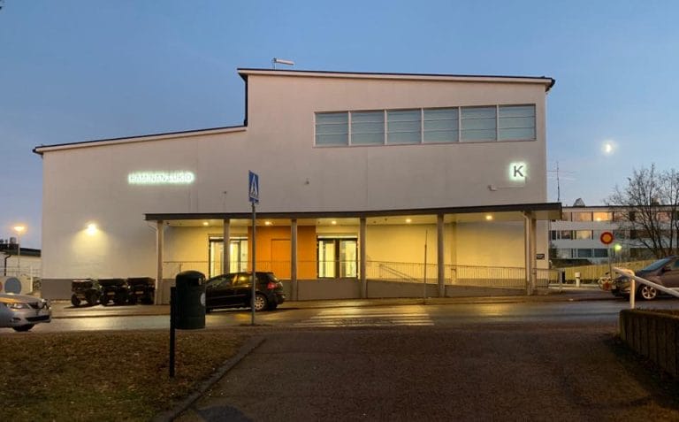 Haminan lukion rakennus iltavalistuksessa pääovi ja koulun nimi valaistuna.