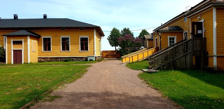 Keltaisia puurakennuksia ja piha.