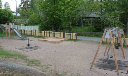 Leikkipaikka, jossa aita, liukumäki, keinuja, kieputin ja hiekkalaatikko.