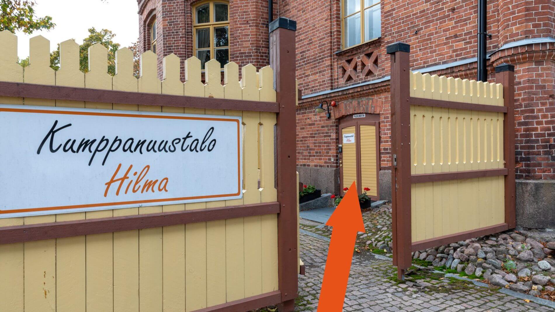 Kumppanuustalo Hilman keltainen aita ja sisäänkäynti merkattu oranssilla nuolella.