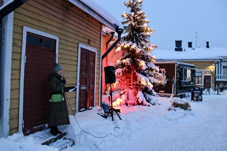 Taustalla joulukuusi, edustalla nainen puhumassa mikrofoniin.