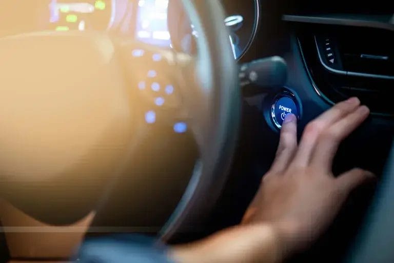 Käsi painamassa auton käynnistysnappia.