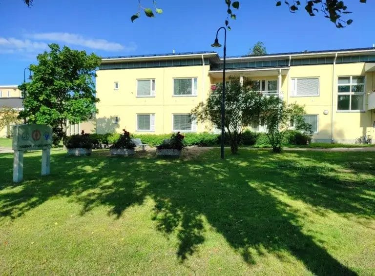 Keltainen rakennus vehreän nurmen ja puiden keskellä.