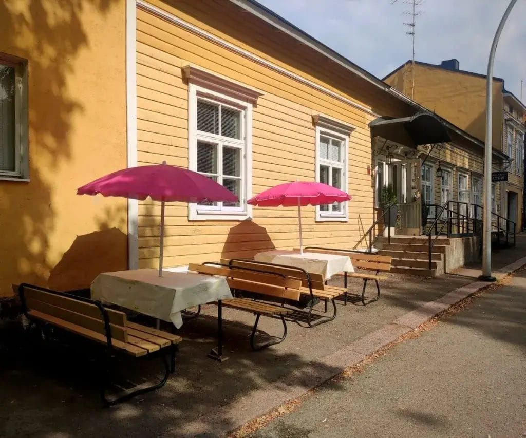 Keltaisen puurakennuksen edessä kaksi puutarhapöytää.