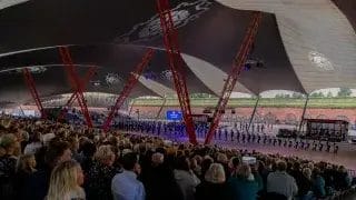 Ihmisiä istumassa katsomossa Hamina Bastionin telttakatoksen alla. Kentällä sotilassoittajien ryhmä.