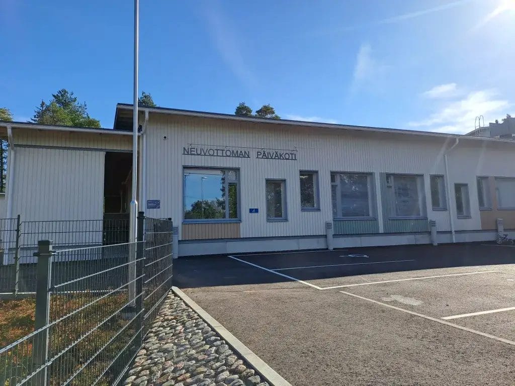 Kuvassa Neuvottoman päiväkodin julkisivu, asfaltoitua pihaa ja aitaa