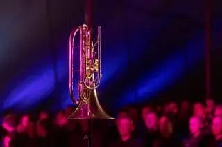 Puhallinsoitin etualalla ja taustalla ihmisiä valaistuna.