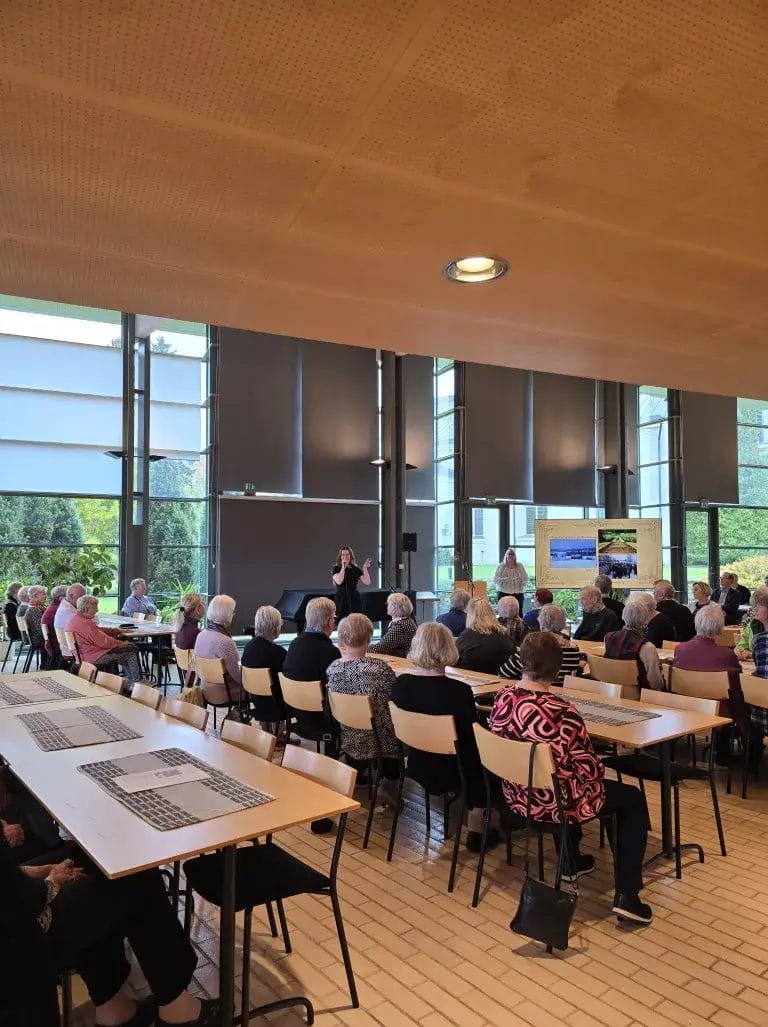 Ihmisiä istumassa pöydässä ja kuuntelemassa laulajaa.