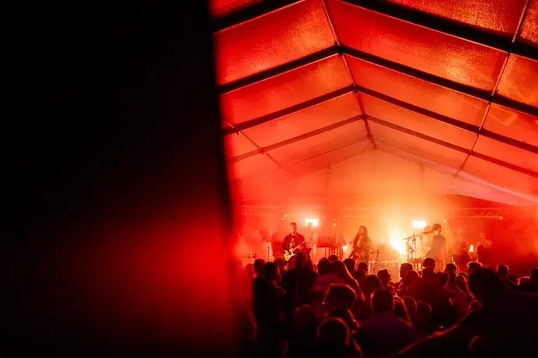 Oranssi tapahtuma teltta, jossa ihmisiä lavan edessä.