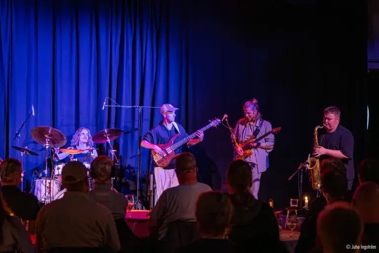 Soittajia lavalla sinisessä tunnelmavalaituksessa yleisön edessä.