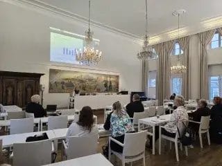 Ihmisiä istumassa selin kamaraan pöytien ääressä.