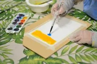 Käsi, jossa sivellin maalaamassa vesiväreillä.