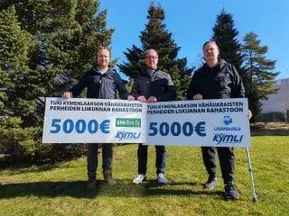 Kolme miestä ulkona kädessään kaksi 5000€ lahjoitusplanssia.